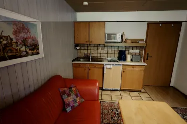 Eine gemütliche Küche mit einer roten Couch, einem Esstisch und Holzschränken. Die Wände sind hell, und es gibt ein Kunstwerk neben der Couch.