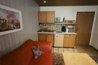 Eine gemütliche Küche mit Holzschränken und modernen Geräten. Auf der linken Seite befindet sich ein rotes Sofa mit einem bunten Kissen.