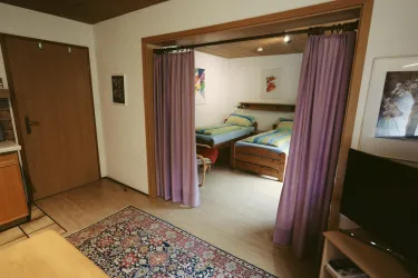 Ein gemütliches Zimmer mit zwei Betten und farbenfrohen Decken. Vor dem Zimmer befindet sich ein Teppich und ein Fernseher.