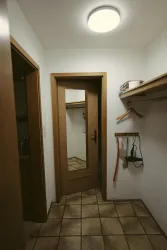 Ein heller Flur mit einem großen Spiegel und einer Holzablage. An der Wand hängen einige Utensilien und ein Kleiderhaken.