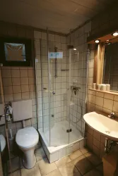 Ein modernes Badezimmer mit einer Glasdusche und einem Waschbecken. Die Wände sind gefliest und es gibt eine Toilette sowie einen Spiegel.