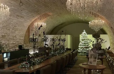 Ein festlich dekorierter Raum mit einem Weihnachtsbaum und eleganten Kristallleuchtern. Der Tisch ist mit Lichtern und Pflanzen geschmückt.