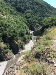 Eine schmale Schlucht mit grün bewaldeten Hängen. Ein kleiner Fluss schlängelt sich durch die Landschaft.