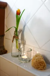Eine schöne Glasflasche mit einer Tulpe und ein Teelicht auf einer Ablage. Daneben liegt ein Schwamm.