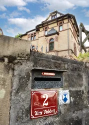 Ein historisches Gebäude mit einem auffälligen, oberen Giebel ist im Hintergrund zu sehen. Im Vordergrund befindet sich ein Briefkasten mit der Nummer 2 und der Aufschrift "Alter Viehberg".