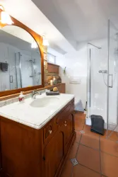 Ein modernes Badezimmer mit einem Holzwaschtisch und einem großen Spiegel. Die Dusche ist mit Glas abgetrennt und der Boden hat terrakotta Fliesen.