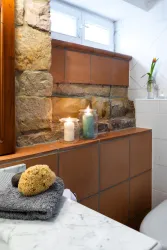 Ein modernes Badezimmer mit einer Kombination aus Stein- und Fliesenwänden. Auf der Ablage stehen Kerzen und ein Schwamm, was eine entspannende Atmosphäre schafft.