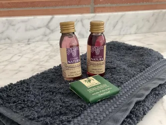 Zwei Flaschen Shampoo und Duschgel auf einem dunklen Handtuch. Daneben liegt eine Seife mit grünem Verpackung.