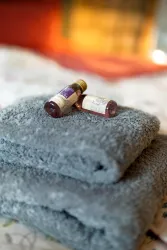 Zwei graue Handtücher liegen übereinander, neben ihnen befinden sich zwei Fläschchen mit ätherischen Ölen. Die Umgebung wirkt gemütlich und entspannend.