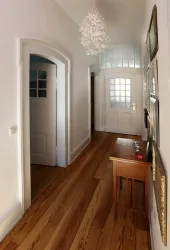 Ein heller Flur mit Holzfußboden und weißen Wänden. An der Wand hängen Bilder, und ein kleiner Tisch steht neben der Tür.