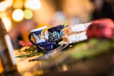 Zwei Tassen stehen auf einem Tisch neben leicht geschnittenem Brot. Im Hintergrund sind unscharfe Lichter zu sehen, die eine gemütliche Atmosphäre schaffen.