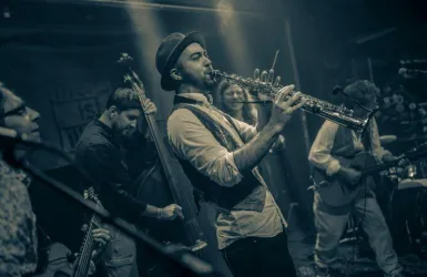 Eine Band spielt live auf der Bühne. Ein Musiker bläst Saxophon, umgeben von anderen Instrumentalisten.