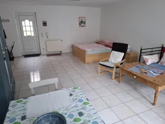 Ein schlichtes Zimmer mit zwei Betten und einem Tisch. Die Wände sind hell und der Boden ist gefliest.