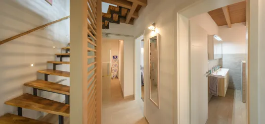 Ein moderner Flur mit Holztreppe und hellen Wänden. In der Nähe befindet sich ein Badezimmer mit modernen Armaturen.