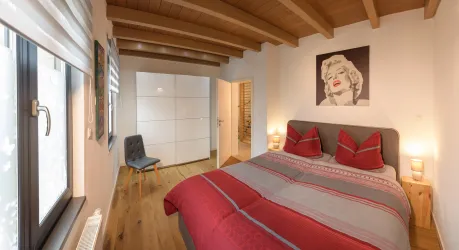 Ein gemütliches Schlafzimmer mit einem großen Bett und roten Kissen. An der Wand hängt ein Bild von Marilyn Monroe, und es gibt einen hellen Holzboden.