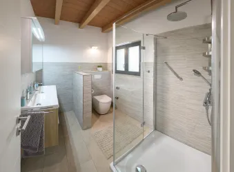Ein modernes Badezimmer mit einer begehbaren Dusche und einer stilvollen Badewanne. Die Holzdecke und die neutralen Farben verleihen dem Raum eine helle und einladende Atmosphäre.