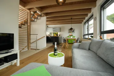 Ein modernes Wohnzimmer mit einem gemütlichen grauen Sofa und einem Kaffee-Tablett. Der Raum hat eine offene Küche im Hintergrund und große Fenster, die viel Licht hereinlassen.