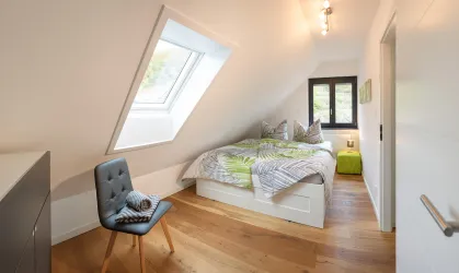 Ein gemütliches Schlafzimmer mit zwei Betten und hellen Farben. Es gibt ein Fenster mit Dachschräge und einen Stuhl in der Ecke.