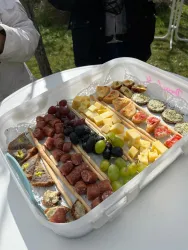 Ein hübsches Tablett mit verschiedenen Snacks, darunter Wurst, Käse, Trauben und Obst. Die Anordnung ist farbenfroh und einladend.