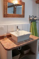 Ein modernes Badezimmer mit einem eleganten Waschbecken auf einer Steinarbeitsplatte. Der Holzrahmen des Spiegels und die dekorativen Körbe verleihen dem Raum einen warmen, einladenden Charakter.