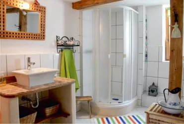 Ein modernes Badezimmer mit einer Dusche und einem Waschbecken. Es enthält helle Fliesen und dekorative Elemente wie ein handgemachtes Regal und einen farbigen Badteppich.