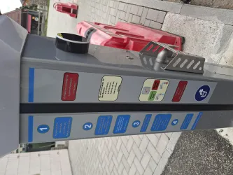 Ein Parkautomaten mit verschiedenen Bedienungshinweisen. Im Hintergrund sind rote Absperrungen zu sehen.