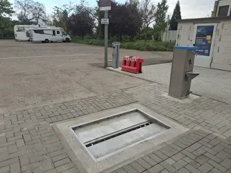 Ein Parkplatz mit einem Entsorgungsbereich für Camper. Im Vordergrund ist eine Öffnung für Abwasser zu sehen, daneben ist ein Wasseranschluss.