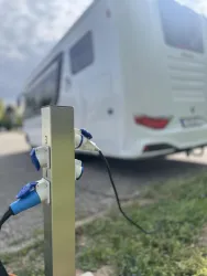 Eine Ladestation für Wohnmobile steht im Vordergrund. Im Hintergrund ist ein weißes Wohnmobil sichtbar.