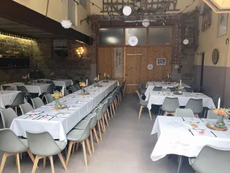 Ein stilvoll eingerichteter Essbereich mit langen Tischen und eleganten Stühlen. Kerzen und Blumen schmücken die Tische in einem freundlichen Ambiente.