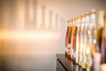 Eine Reihe von Flaschen mit Getränken steht auf einem Tisch. Die Flaschen werfen interessante Schatten auf die Wand.