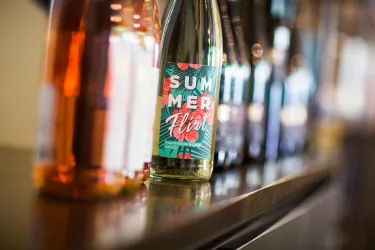 Eine Reihe von Weinflaschen steht auf einem Tisch. Im Vordergrund ist eine Flasche mit dem Etikett "SUMMER FIZZ" zu sehen.