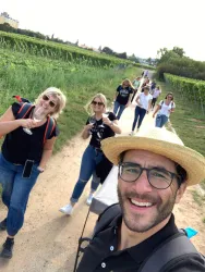 Eine Gruppe von Menschen wandert auf einem Weg durch Weinberge. Einige Personen lächeln und posieren für ein Foto.