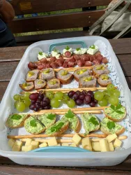 Ein platter Snack mit verschiedenen belegten Broten, Trauben und Käse. Die Auswahl umfasst herzhaftes und frisches Gemüse, ideal für eine Feier.