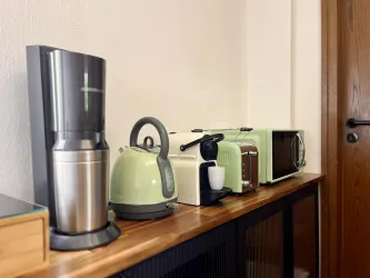 Eine moderne Küchenzeile mit verschiedenen kleinen Haushaltsgeräten. Dazu gehören eine Kaffeemaschine, ein Wasserkocher, ein Toaster und eine Mikrowelle in einem harmonischen Farbton.