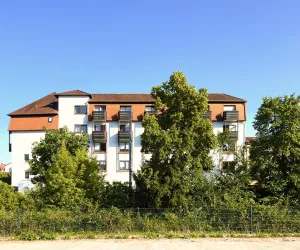 Ein modernes Gebäude umgeben von Bäumen und Sträuchern. Der Himmel ist klar und blau.