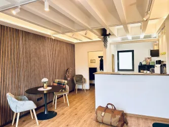Ein modernes, helles Raumambiente mit Holzvertäfelung und eleganter Einrichtung. Der Bereich enthält einen Tisch, Stühle und eine Kaffeeküche.