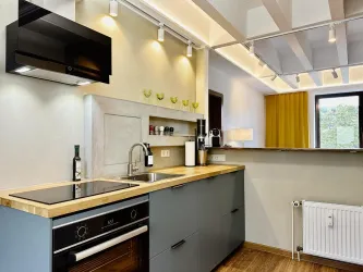 Eine moderne Küche mit einer Holzarbeitsplatte und integrierten Geräten. Viel Licht und eine elegante Farbgestaltung schaffen eine einladende Atmosphäre.
