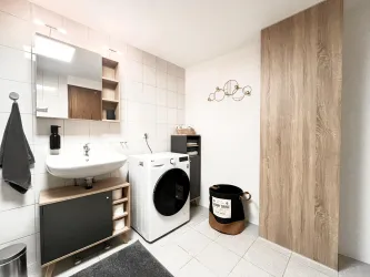 Ein modernes Badezimmer mit einer Waschmaschine und einem Waschbecken. Es gibt einen Holzschrank und dekorative Elemente an der Wand.