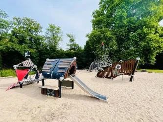 Ein moderner Spielplatz mit verschiedenen Klettergerüsten und einer Rutsche. Die Umgebung ist grün und sonnig, ideal für Kinder.