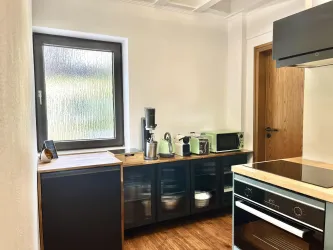 Eine moderne Küche mit Holzmöbeln und verschiedenen Küchengeräten. Das Fenster lässt viel Licht herein und sorgt für eine helle Atmosphäre.