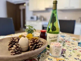 Ein schöner Tisch mit einer Dekoration aus Tannenzapfen, einem Eiermotiv und einer blühenden Pflanze. Im Hintergrund steht eine Flasche Wein und ein Glas mit Kerzen.