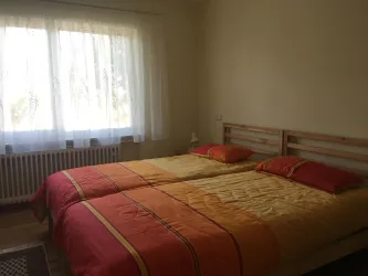 Schlafzimmer mit einem Doppelbett, die auch einzeln stehen können. Das Zimmer hat ein großes Fenster mit viel Tageslicht.