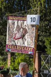 Eine bunte Fahne mit traditionellen Figuren und dem Schriftzug "Neustadt". Die Fahne wird von einem Mann auf einer Veranstaltung gehalten.