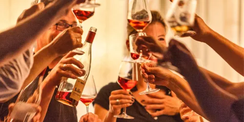 Eine Gruppe von Menschen hebt Gläser mit Wein zur Feier. Die Stimmung ist fröhlich und gesellig.