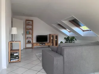 Ein moderner Wohnraum mit schrägen Dachfenstern - hell und freundlich eingerichtet, mit einem TV-Schrank und einer Lampe.
