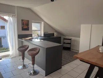 Eine moderne Küche im Dachgeschoss mit stilvollen Barhockern. Es gibt eine helle Fensterfront und gemütliche Dekoration.