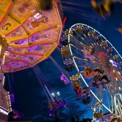 Ein lebhaftes Herbstfest mit einem Riesenrad und einem Karussell. Die Lichter leuchten hell gegen den nächtlichen Himmel.