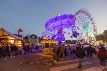 Ein Jahrmarkt mit einem bunten Karussell und einem riesigen Riesenrad. Viele Menschen genießen die festliche Atmosphäre am Abend.
