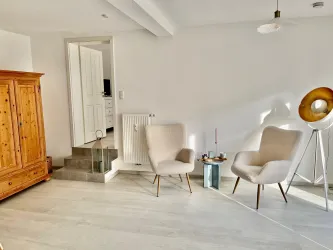 Ein heller, einladender Raum mit zwei bequemen Stühlen und einer Holzkommode. Die Einrichtung ist modern und minimalistisch.