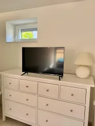 Ein modernes Wohnzimmer mit einer weißen Kommode. Auf der Kommode stehen ein Fernseher und eine Tischlampe.